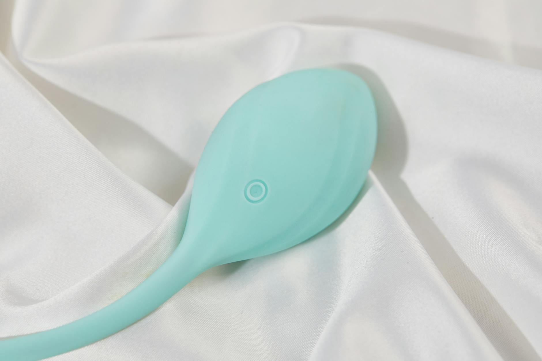 A sleek teal lemon clitoral vibrator resting on soft white silk fabric