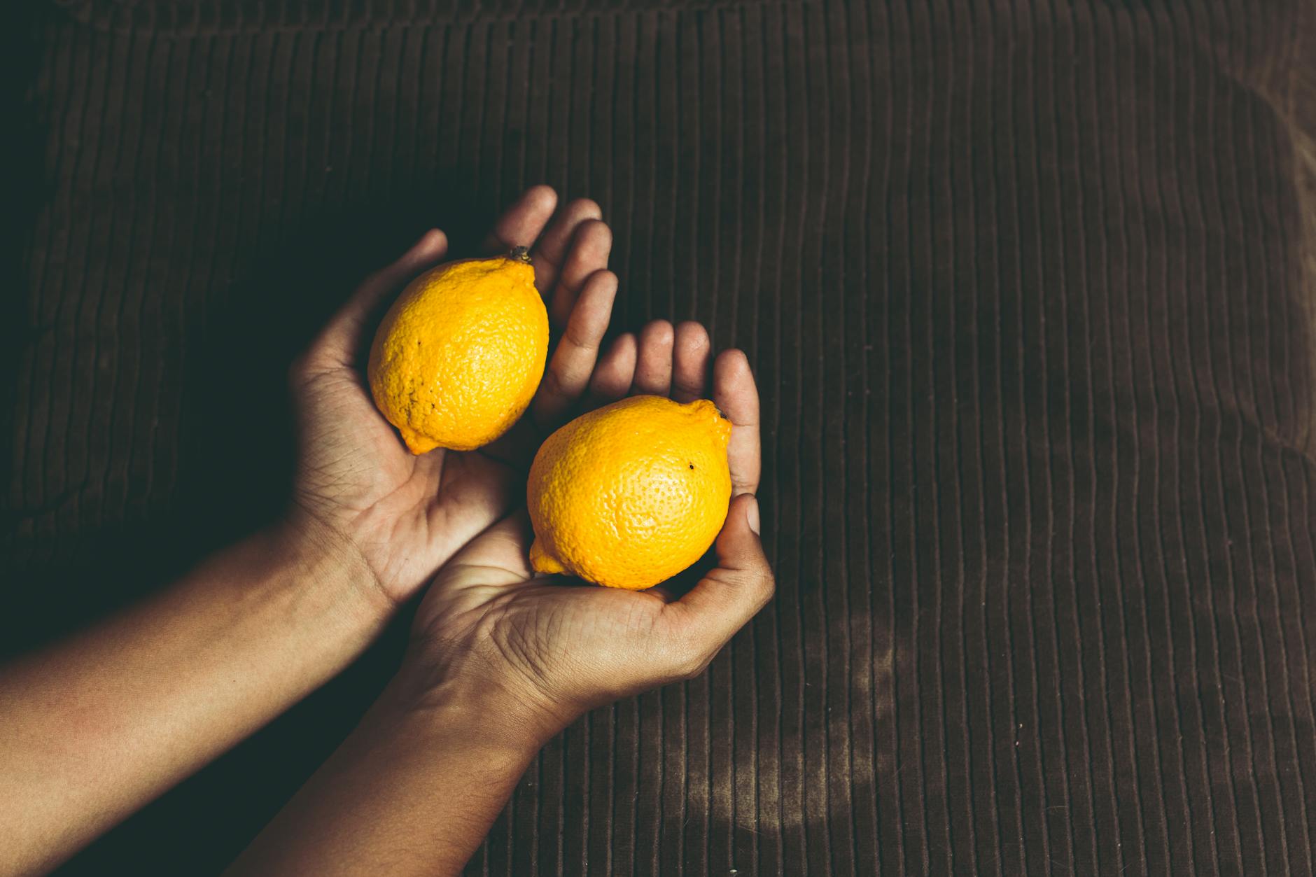 Close-up of two fresh lemons held in cupped hands on a brown surface, symbolizing freshness and renewal