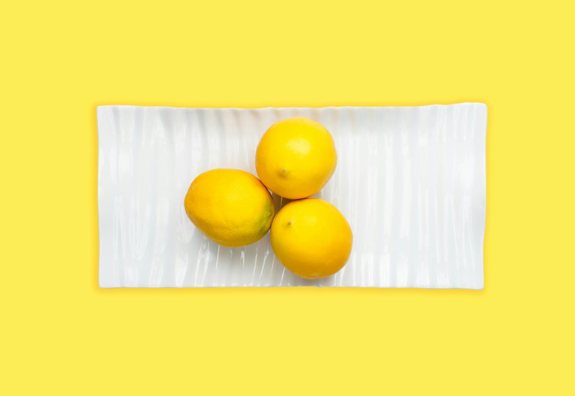 Fresh lemons arranged on white plate with vibrant yellow background, symbolizing the lemon clitoral vibrator design