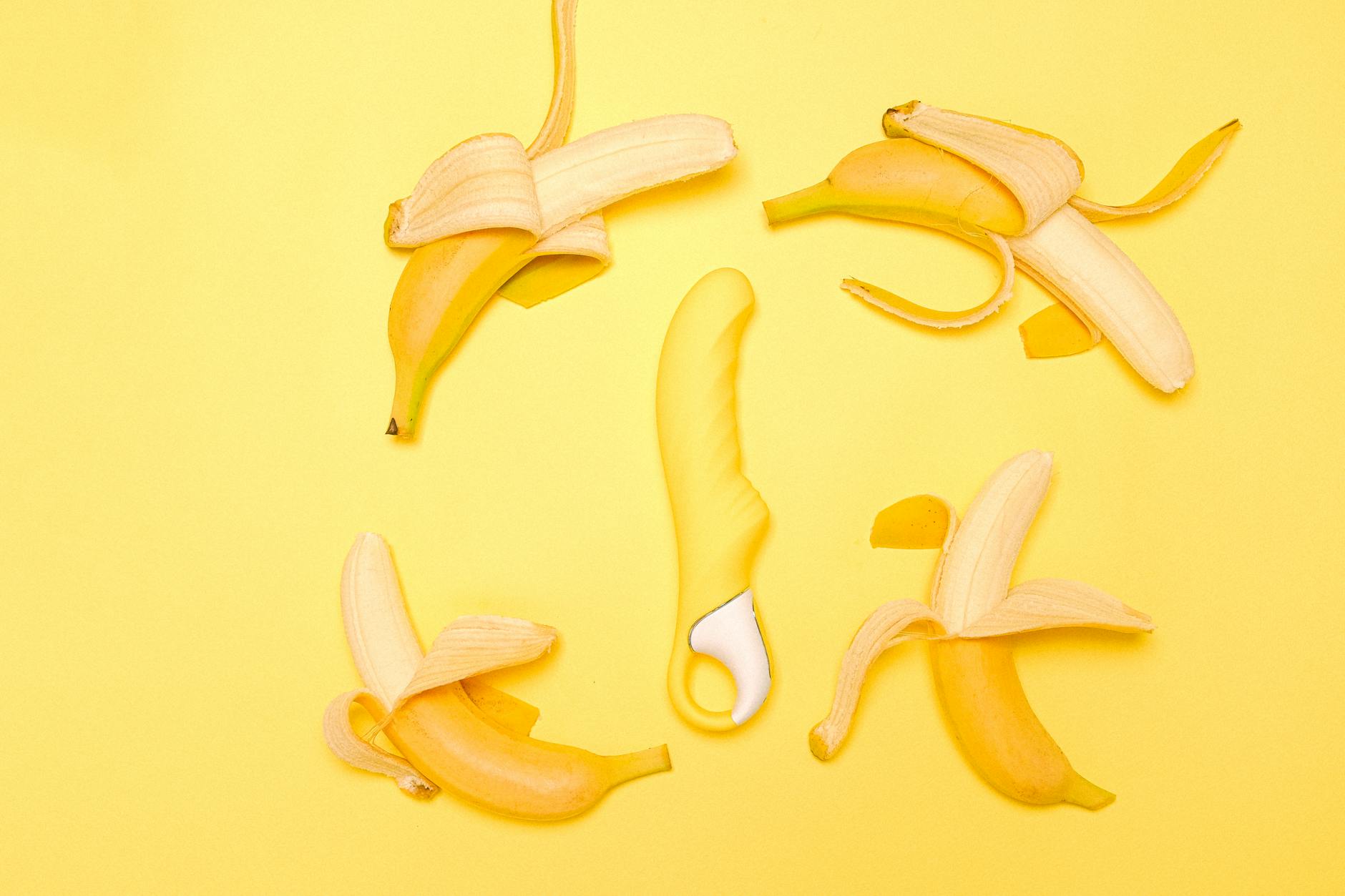 Yellow lemon vibrator surrounded by fresh lemons and bananas on a bright yellow background