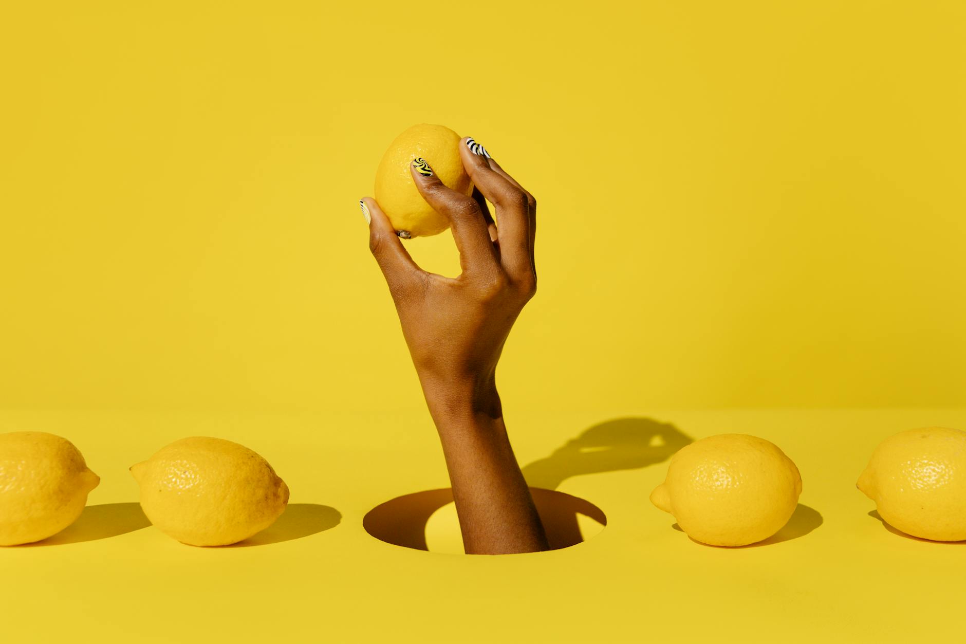 A hand holding a lemon against a vivid yellow background, symbolizing fresh citrus energy and stress relief